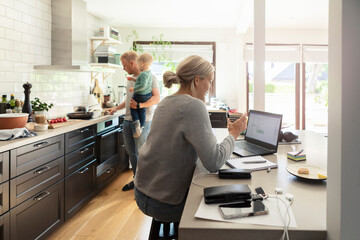 Mother using laptop while father cooking with son in kitchen