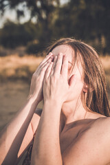 Long-haired woman covers her face with both hands in a gesture of sorrow, desolation or sadness....