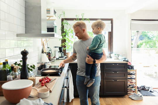 Father carrying son while cooking food in kitchen