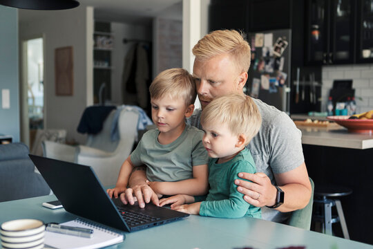 Father using laptop sitting with children in living room