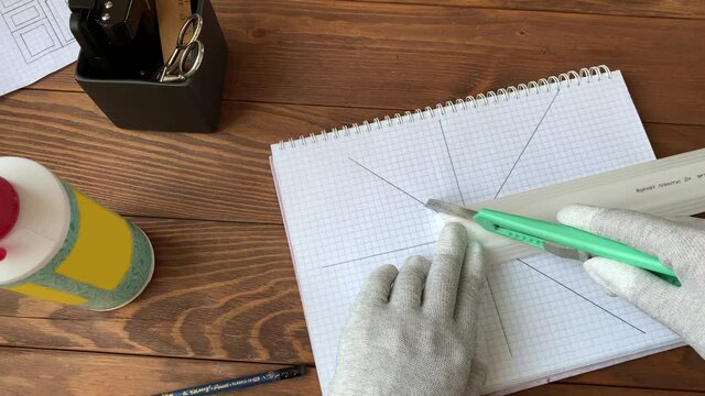 Human's hands wearing work gloves cut molding with stationery knife. On sketched notebook woman trims ceiling skirting board. Interior designer workplace. Diy handicraft.