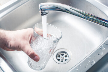 Hand Holding A Drinking Glass Over Kitchen Sink Filling It With Water Streaming From Faucet
