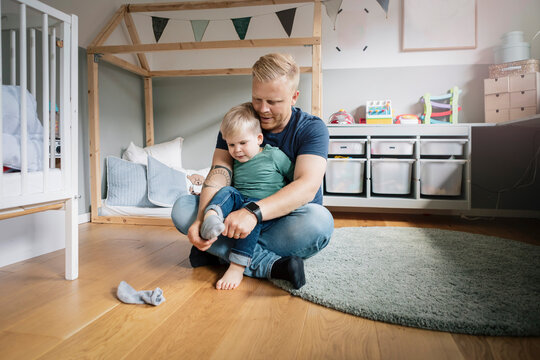 Father helping son to wear socks in bedroom
