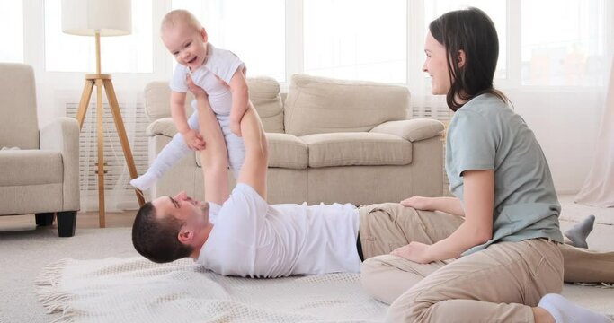 Parents having fun playing with baby son lying on carpet at home