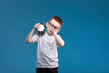 Little boy waking up with alarm clock, isolated on the blue background. Define your own rhythm of life. Happy hours concept. Schedule and timing