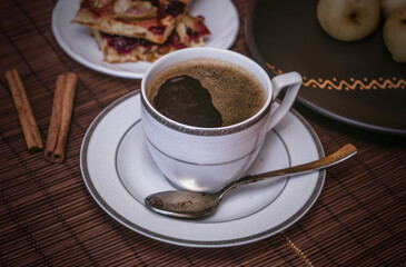 Still life - a hot cup of black coffee, homemade cookies with fruit, baked apples on a bamboo mat