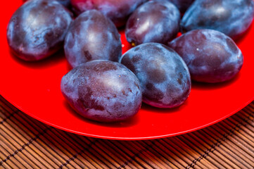 Large fresh purple plum fruits with on a bamboo mat, still life, close-up