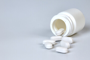 White bottle with scattered white tablets on a gray background