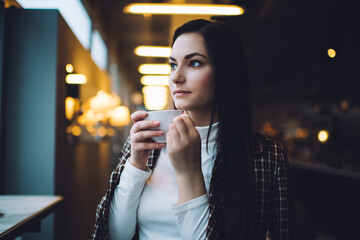 Thoughtful young woman drinking hot coffee in cafeteria
