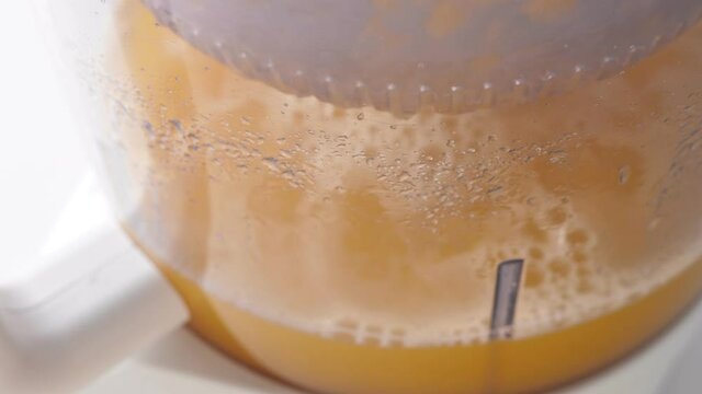 Preparing orange juice in juicer. Squeezing procces. Macro shot inside transparent bowl