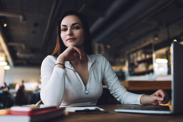 Dreamy woman with laptop in cafeteria