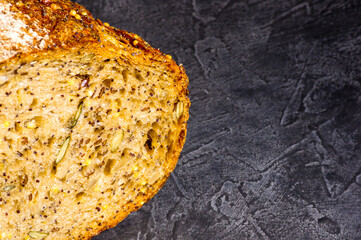 Slice of rustic natural yeast-free bread with flax, poppy seeds, sesame seeds, millet, pumpkin and sunflower seeds, on a black background, hard light, photo in a low key, close up.
