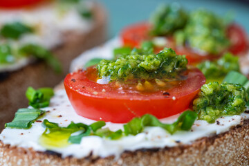 Delicious toasted bread with white cream cheese, green wild garlic and tomato on plate, close up