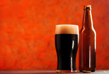 A pint glass of dark craft beer stout or porter from a bottle. Creative orange background, copy space - obrazy, fototapety, plakaty