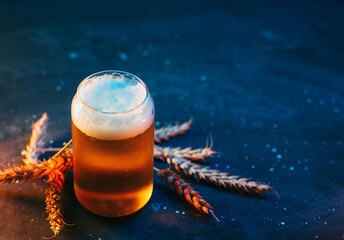Stylish creative beer glass on a dark blue background. Ears of wheat. Cold light lager