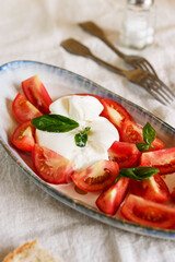 Traditional Italian salad with Burrata cheese, tomatoes and fresh basil. Mozzarella burrata salad with basil leaves and tomatoes on plate on beige linen tablecloth