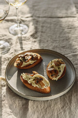 Bruschettas or toasts with cheese and fried mushrooms with thyme served with glasses of wine on greige linen tablecloth