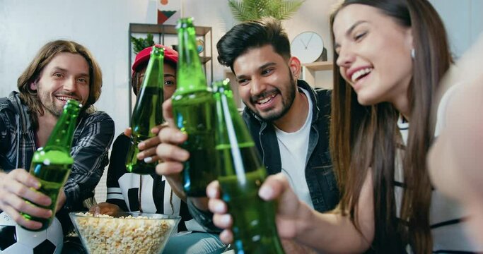 Adorable cheery happy modern young mixed race friends clinking bottles of beer while looking at phone camera to make selfie during party,leisure concept