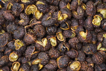 Macro full frame closeup of raw brown whole chinese sichuan timut pepper corns with citrus anise...