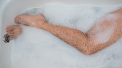 Funny picture of a man taking a relaxing bath. Close-up of male feet in a bubble bath. Top view