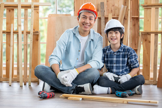 Asian father and son stay in their workplace of carpentering and look at camera with smiling. Asian family concept to stay at home and enjoy good relationship hobby together.