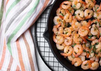 Prawns fried with garlic in a cast iron skillet on a white table with a striped linen napkin. Top view