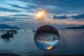 Fototapeta na wymiar The sparkle of burning steel wool is the red line in the glass ball in twilight. .With the sea and the morning light as a background..