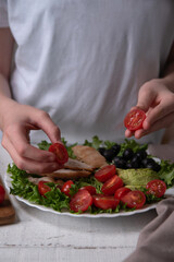 The chef prepares a delicious diet meal of chicken breast, lettuce, avocado, tomatoes.