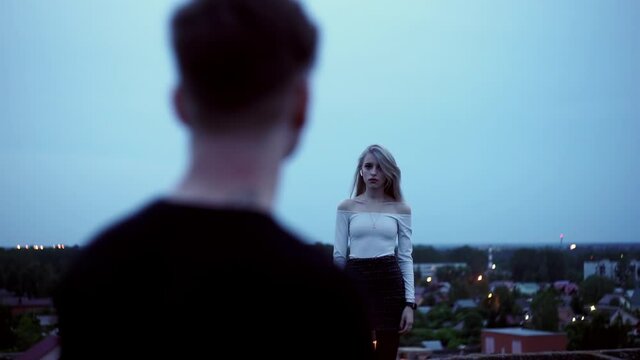 A girl and a guy stand like a fan on the roof and look longingly into each other's eyes. A light breeze is blowing. Emotional shots