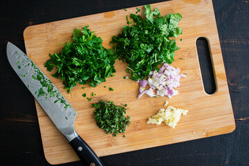 Chopped Herbs on a Bamboo Cutting Board: Chopped parsley, cilantro, oregano, shallots, and garlic...
