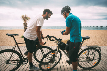Cyclists on a bike on a wooden walkway on the beach with the sea and a bridge in the background looking at the mobile phone. Clear sky background with copy space. sport concept. urban cycling concept
