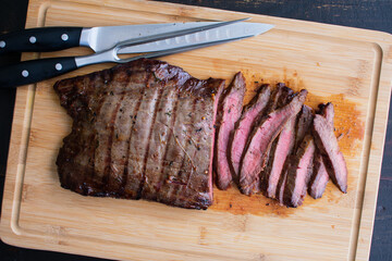 Bourbon Marinated Grilled Flank Steak: Sliced medium-rare flank steak on a bamboo carving board