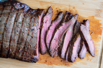 Bourbon Marinated Grilled Flank Steak: Sliced medium-rare flank steak on a bamboo carving board