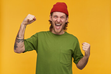 Portrait of happy, adult male with blond hairstyle and beard. Wearing green t-shirt and red beanie....