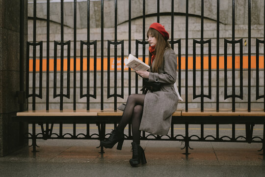 Beautiful Caucasian woman wearing coat, beret and scarf sitting alone on Saint Petersburg metro station reding a book. Image with selective focus and noise effect