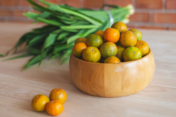 Fresh orange in the wooden bowl put on the wooden table with the pandanus behind. Orange is a healthy fruit and have refreshing sweet taste.