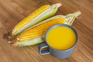 A cup of warm corn soup beside with fresh ear of corn lay down on the table. Corn is a healthy food and versatile use plant. They can use to eat, to make a flour or 
animal feed.
