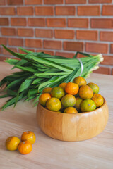 Fresh orange in the wooden bowl put on the wooden table with the pandanus behind. Orange is a...