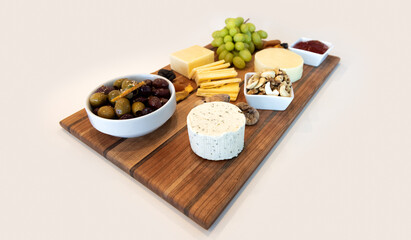 Fototapeta na wymiar Delicious Cheese Assortment on a wooden board with fruit, nuts, jelly, and olives. Gourmet Charcuterie Arrangment.