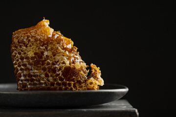 Honeycomb and honey dipper with liquid honey. Selective focus. Dark background, studio image. Organic vegan raw dessert. Copy space. bee products by organic natural food. Beekeeping advertisement. 