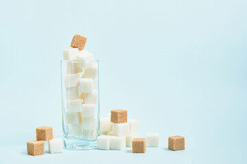 cubes of white and brown sugar in a glass and on a light blue and beige background copy space