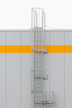 Die Wand einer Industriehalle ziert einen gelben Streifen und eine Au&szlig;entreppe f&uuml;hrt auf das Hallendach.