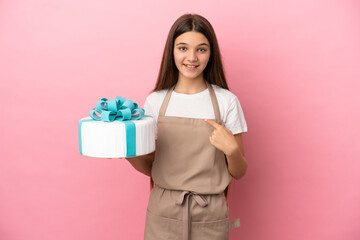 Little girl with a big cake over isolated pink background with surprise facial expression