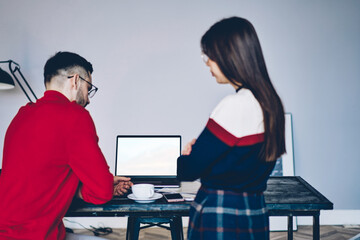 Side view of skilled male and female bloggers collaborating near table with mock up laptop computer, Caucasian business persons discussing freelance project talking near blank netbook with copy space