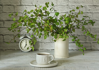 A bouquet of birch branches in a ceramic vase on the background of a white brick wall.