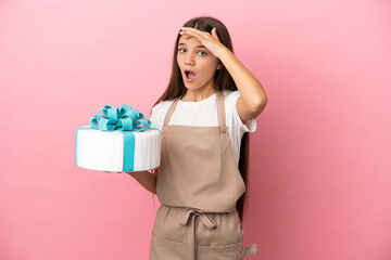 Little girl with a big cake over isolated pink background doing surprise gesture while looking to the side