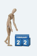 day of the month 22 February calendar . A calendar date on blue cubes and a wooden man standing next to it. White background