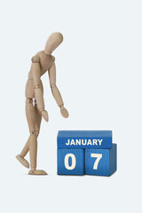 day of the month 07 January calendar . A calendar date on blue cubes and a wooden man standing next to it. White background