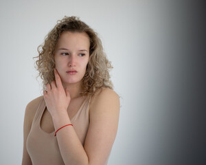 Smart girl, curly hair, hand touches the chin, beige bodysuit, close-up, beauty studio photoshoot, background light gray