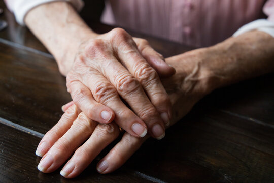 A pair of elderly woman grandmother's hands folded and laying on top of each other.